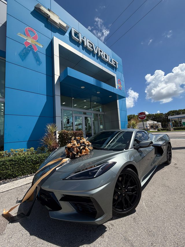 Gray 2024 Corvette C8 with a delivery bow at a Chevrolet dealership